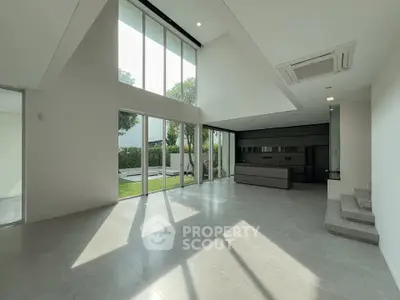 Spacious modern living room with high ceilings and large windows overlooking a lush garden.