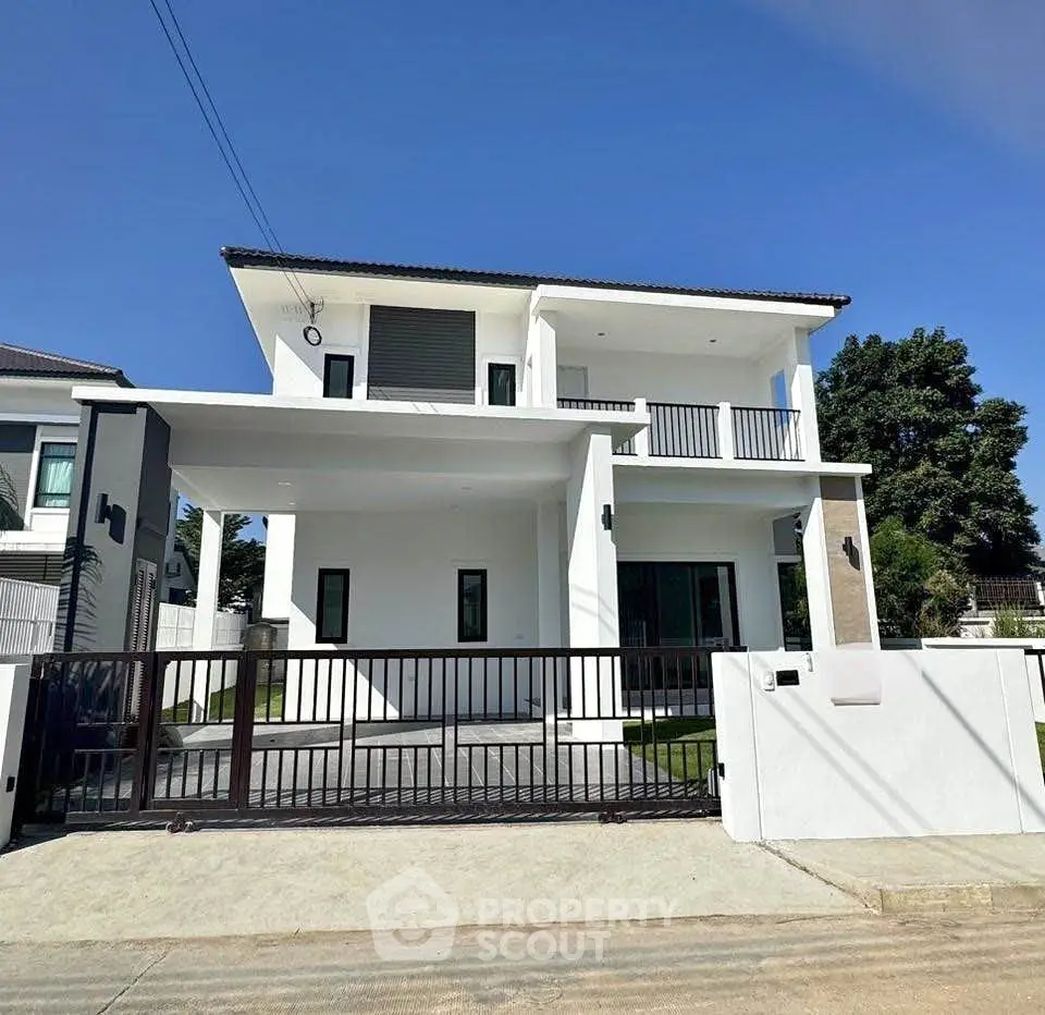 Modern two-story white house with balcony and gated entrance under clear blue sky.