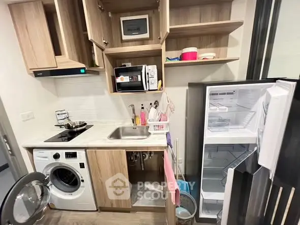 Compact kitchen with modern appliances including washing machine and open fridge.
