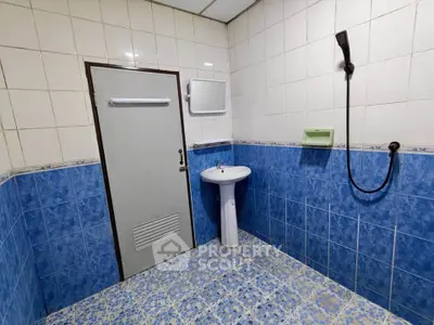 Spacious bathroom with blue and white tiles, featuring a pedestal sink and shower area.