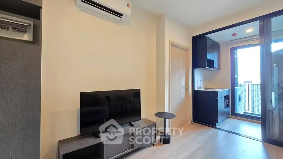 Modern living room with TV and open kitchen leading to balcony with city view.