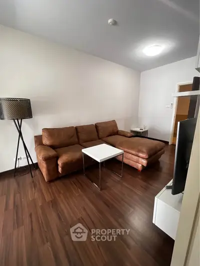 Spacious living room with modern brown leather sofa and sleek wooden flooring.