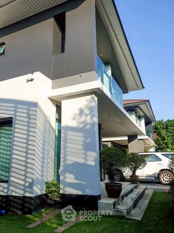 Modern two-story house with sleek design and lush greenery, featuring a spacious balcony and large windows.