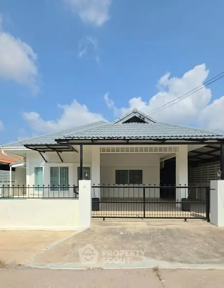 Charming single-story house with a modern roof and gated driveway under a clear blue sky.