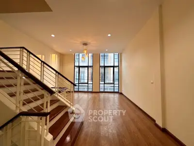Spacious two-level living area with gleaming hardwood floors, large windows allowing ample natural light, and an elegant staircase leading to an upper level, perfect for modern urban living.
