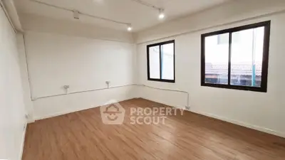 Spacious and well-lit empty room with polished wooden flooring and multiple windows offering ample natural light, ideal for a personalized interior design.
