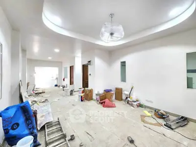 Spacious under-renovation living room with modern ceiling design and ample natural light.