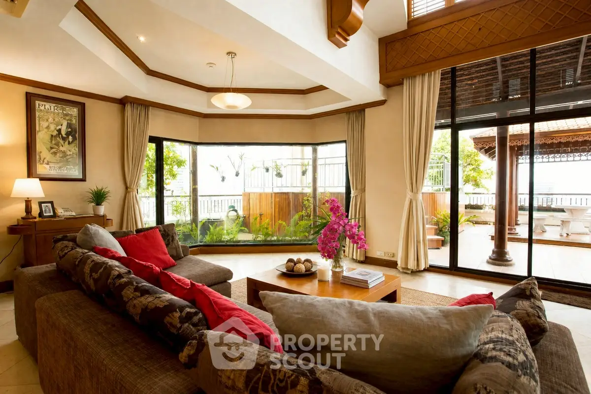 Luxurious living room with large windows and elegant decor, opening to a spacious balcony with garden views.