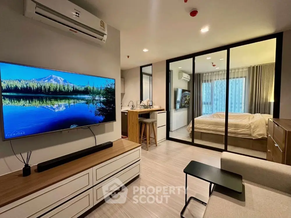 Modern open-plan living room with glass partition to bedroom, featuring sleek furniture and natural light.