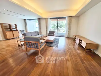Spacious living room with wooden flooring and modern furniture, featuring large windows and natural light.