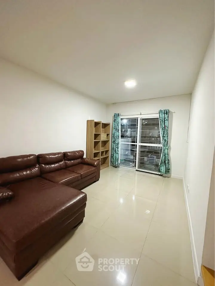 Spacious living room with leather sofa and large window, perfect for relaxation.