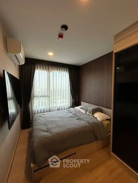 Cozy bedroom with modern decor, large window, and wall-mounted TV in a stylish apartment.