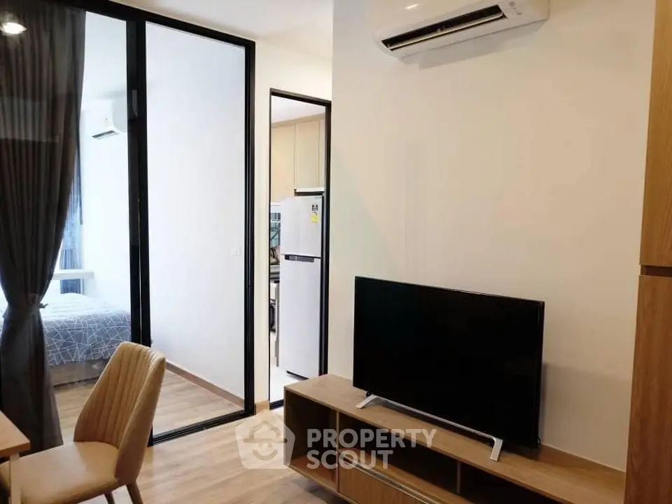 Modern living room with TV, air conditioning, and view into bedroom and kitchen.