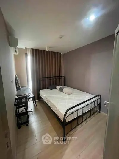 Cozy bedroom with minimalist decor and natural light, featuring a metal bed frame and wooden flooring.