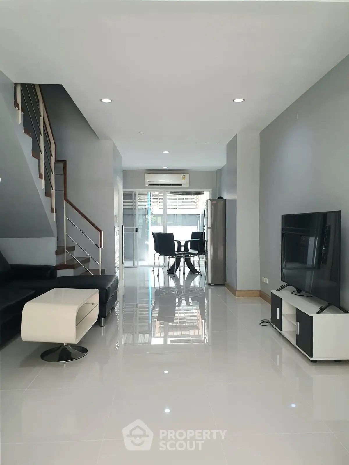 Modern living room with sleek furniture and open dining area, featuring a stylish staircase.