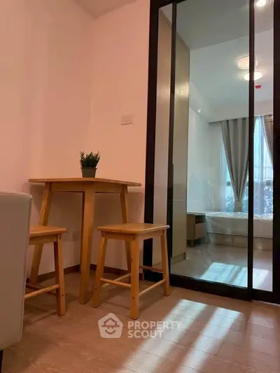 Cozy apartment interior with wooden dining set and view into a bright bedroom through glass doors.