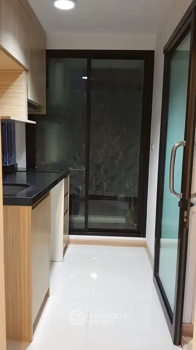 Modern kitchen with sleek cabinetry and glass sliding door, featuring a minimalist design and ample natural light.