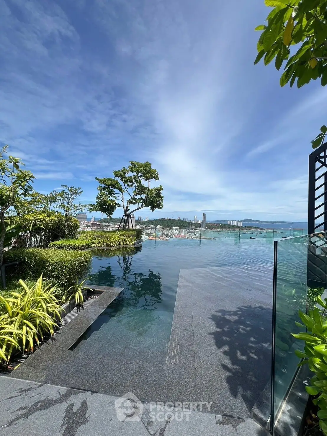 Luxurious rooftop infinity pool with stunning city and ocean views, surrounded by lush greenery.