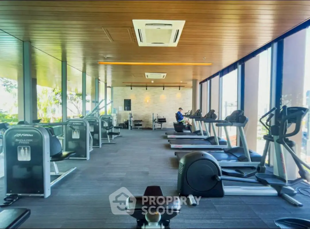 Spacious gym with modern equipment and large windows offering natural light.