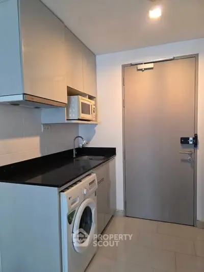Modern compact kitchen with washing machine and microwave in sleek apartment.