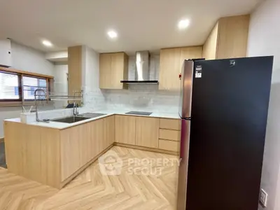 Modern kitchen with sleek wooden cabinetry and black fridge in open layout.