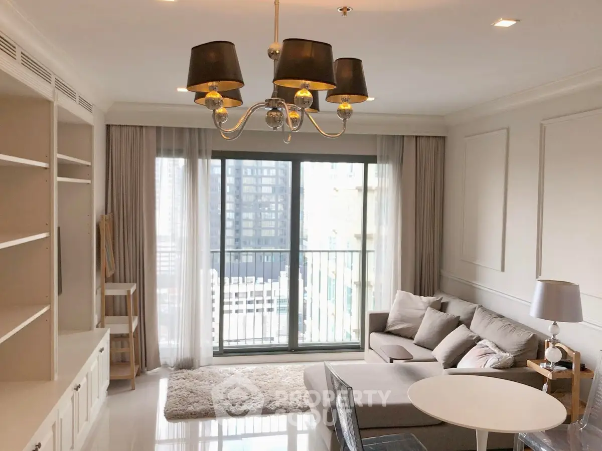 Elegant living room with modern chandelier and city view balcony in luxury apartment.