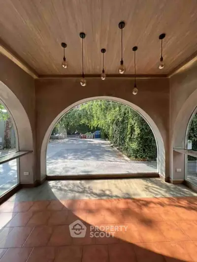 Spacious room with large arched windows offering a serene garden view, perfect for a tranquil living space.