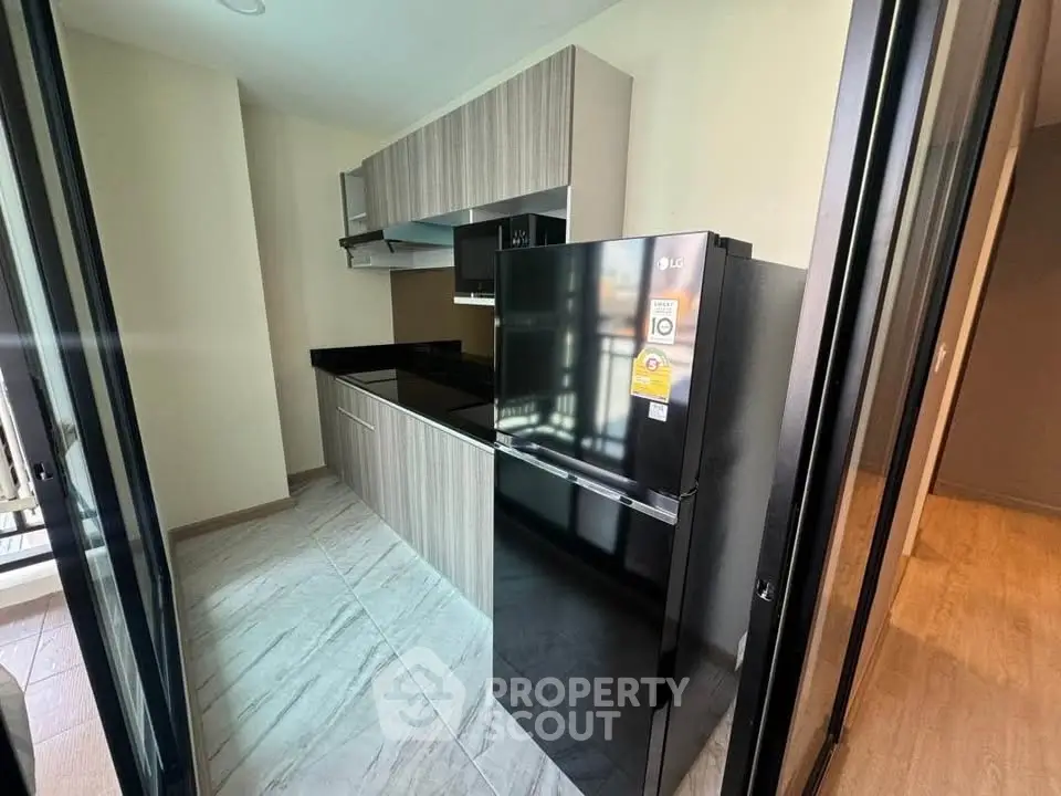 Modern kitchen with sleek cabinetry and black fridge in stylish apartment.