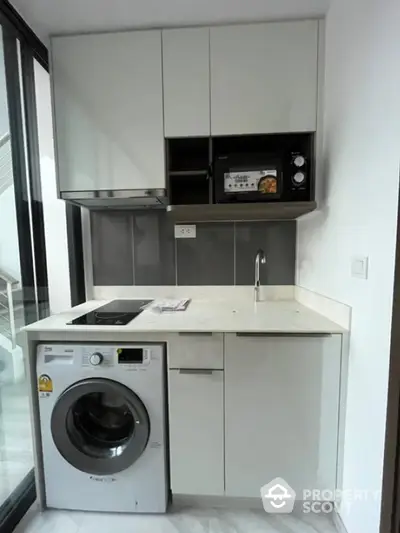 Compact modern kitchen with washing machine and microwave, sleek cabinetry, and minimalist design.