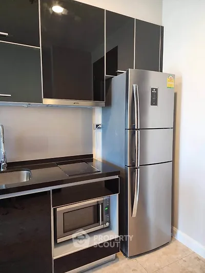 Modern kitchen with sleek black cabinets, stainless steel fridge, and built-in microwave.