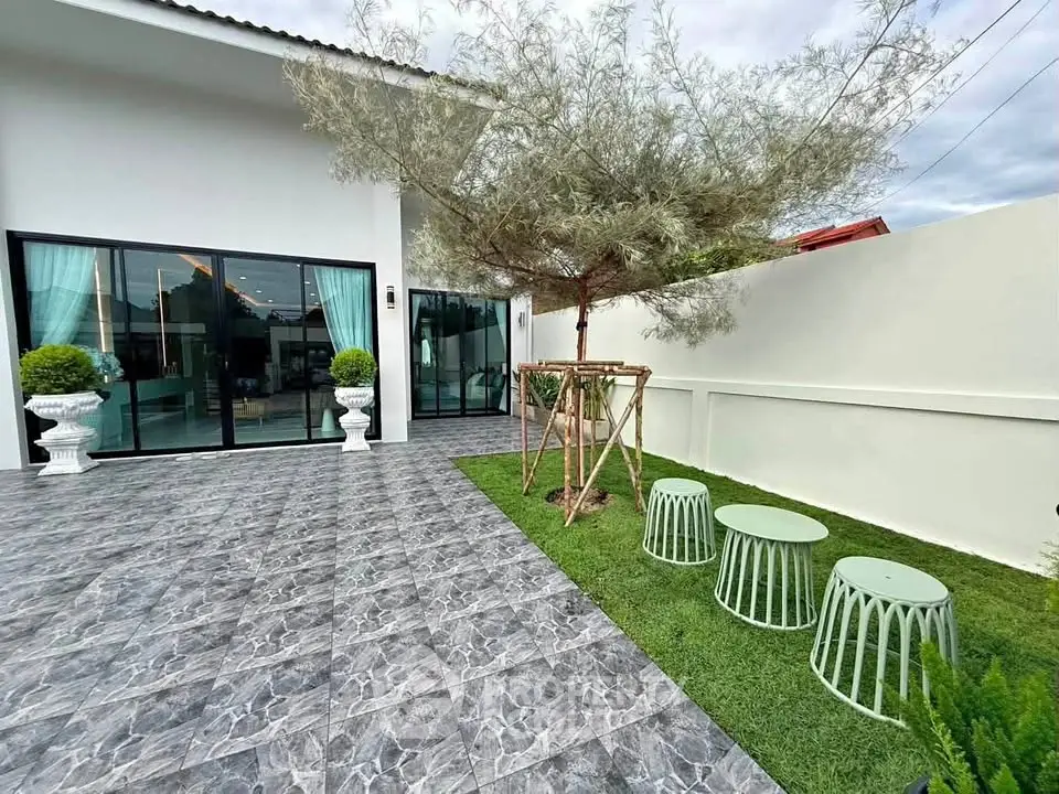 Modern home exterior with stylish patio and lush garden, featuring large glass doors and elegant landscaping.