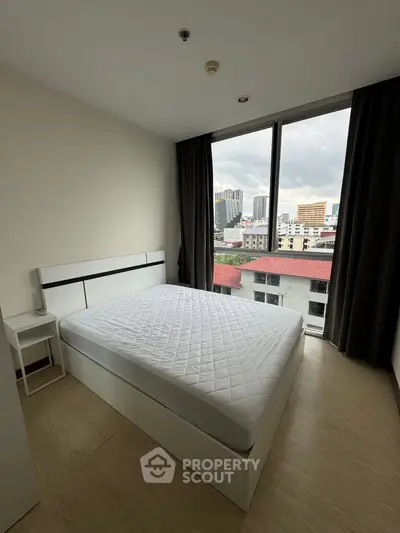 Modern bedroom with large window offering city views, featuring a minimalist design and ample natural light.