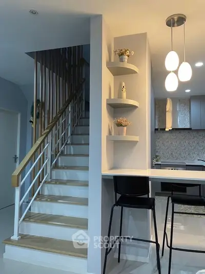 Modern kitchen with stylish open layout and elegant staircase, featuring sleek lighting and contemporary decor.