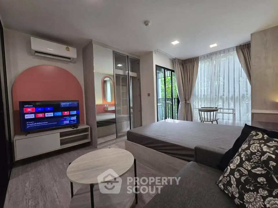 Modern studio apartment with stylish decor, featuring a cozy living area, large windows, and a wall-mounted TV.