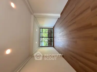 Spacious empty room with wooden flooring and large window offering natural light and greenery view.