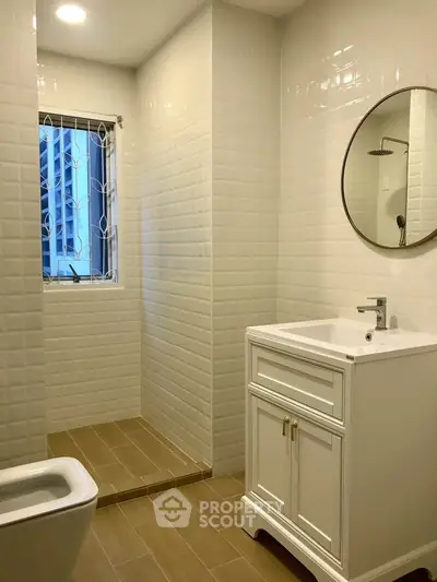 Modern bathroom with elegant white vanity and round mirror, featuring a sleek shower area and natural light.