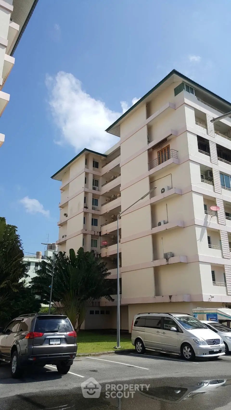 Modern apartment building with spacious balconies and parking area under a clear blue sky.