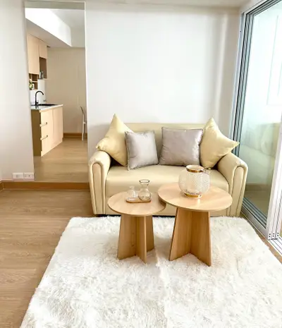 Modern living room with cozy sofa and stylish wooden tables, open kitchen in background.