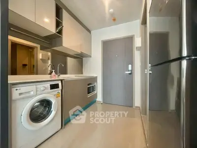 Modern kitchen with sleek cabinets, washing machine, and fridge in compact layout.
