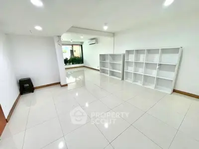 Spacious white-tiled room with built-in shelves and large window, perfect for versatile living space.