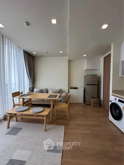 Modern open-plan living room with dining area and kitchen, featuring wooden flooring and natural light.
