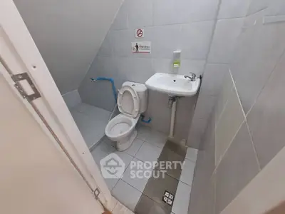 Compact bathroom with modern fixtures and tiled walls, featuring a toilet and sink under a sloped ceiling.