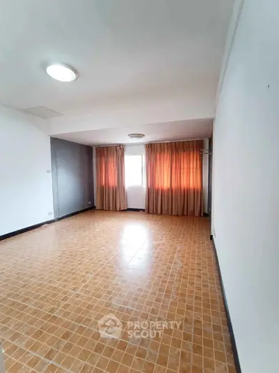 Spacious empty room with tiled floor and large window with curtains, ideal for customization.