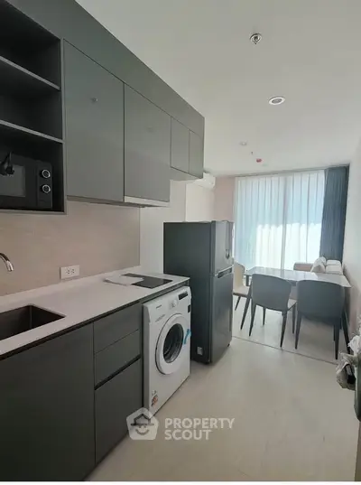 Modern kitchen with sleek cabinets, washing machine, and dining area in open layout.