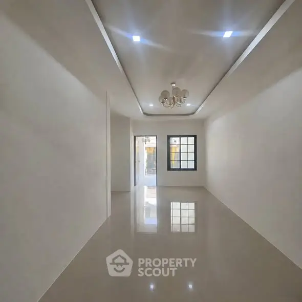 Spacious empty room with glossy floors and modern chandelier, ideal for customization.