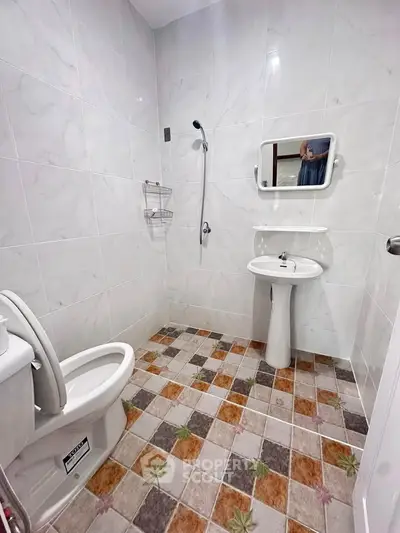 Modern bathroom with tiled walls and floor, featuring a pedestal sink and toilet.