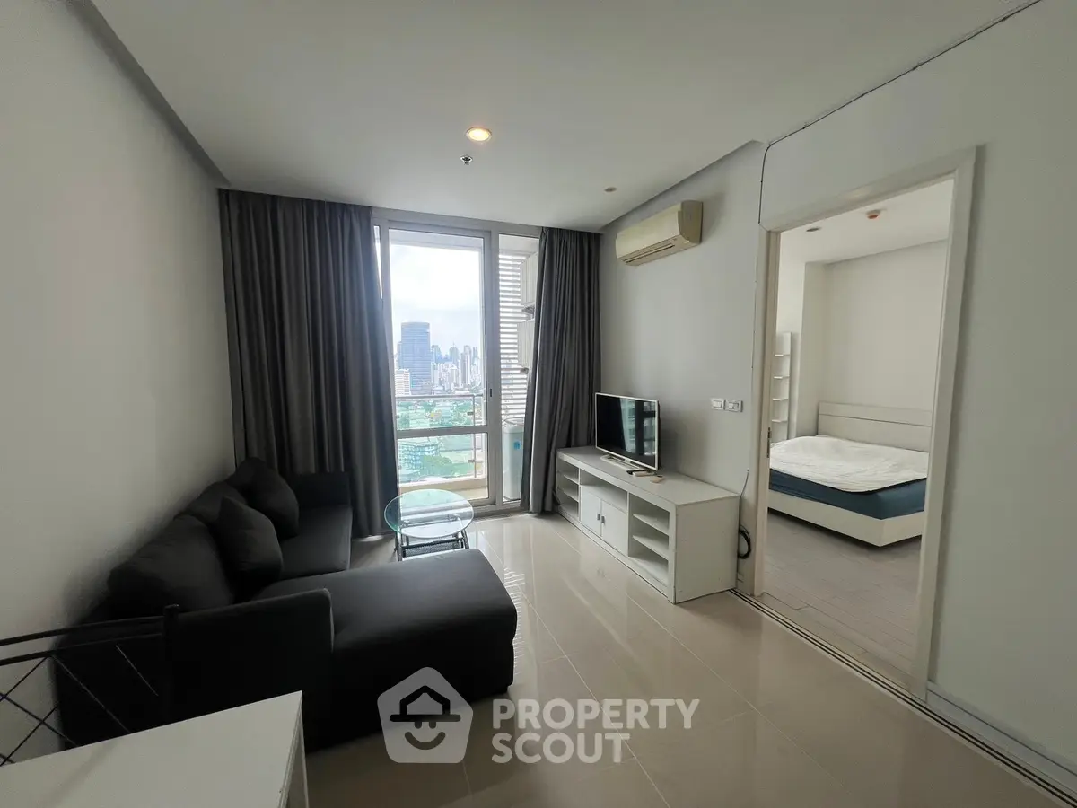 Modern living room with city view, sleek furniture, and natural light in a high-rise apartment.