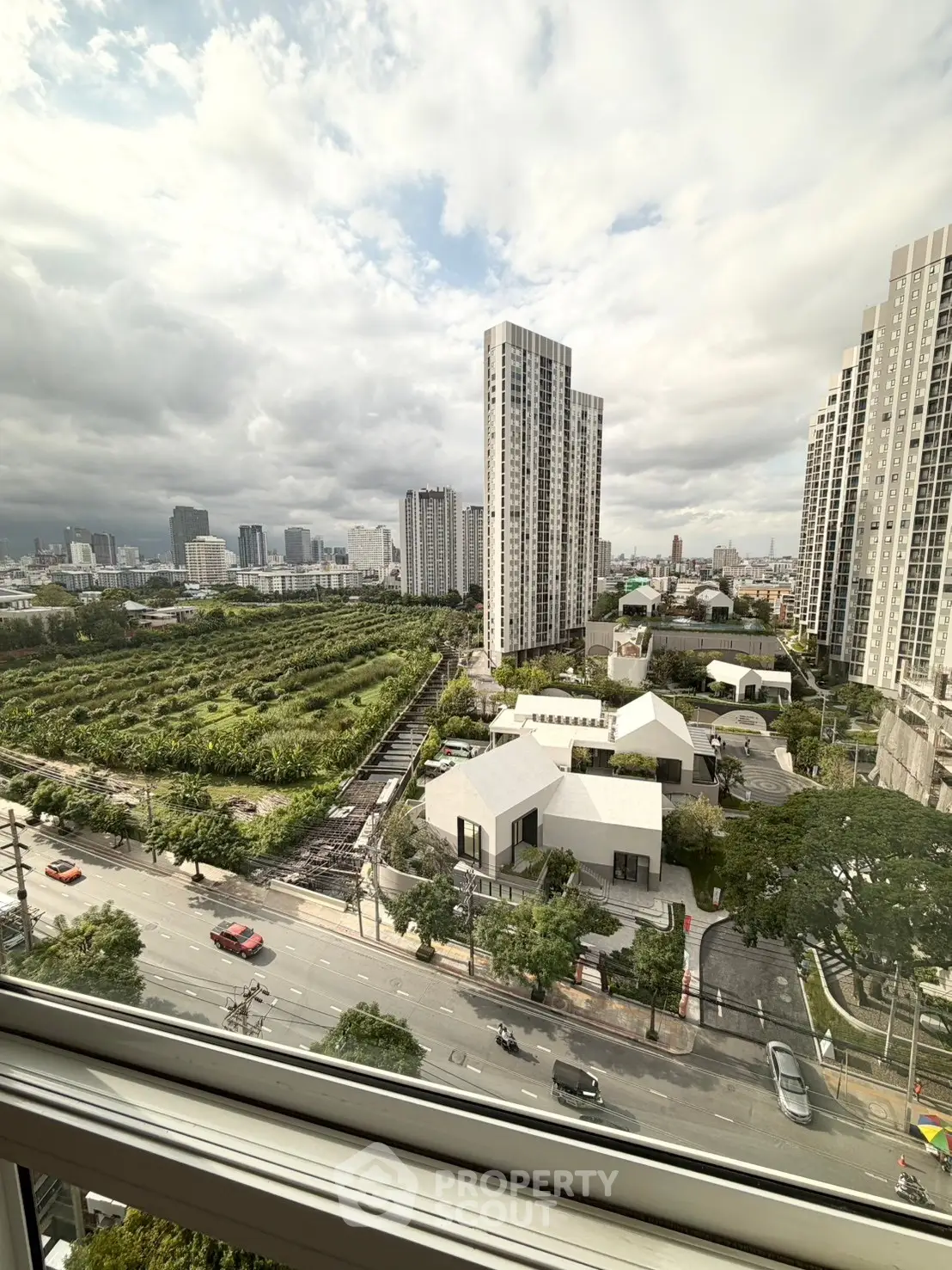 Stunning cityscape view from high-rise apartment window overlooking lush greenery and modern buildings.