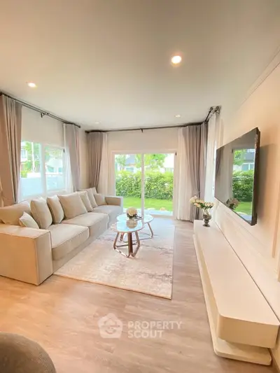 Spacious living room with large windows and elegant decor, offering a serene garden view.