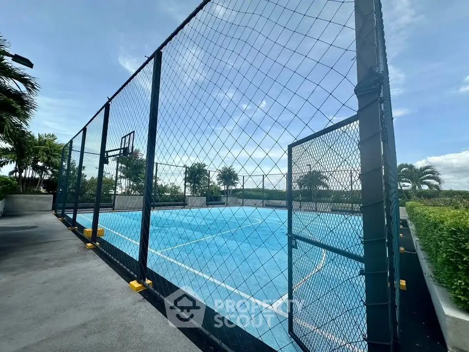 Spacious outdoor basketball court with lush greenery and clear blue skies, perfect for sports enthusiasts.